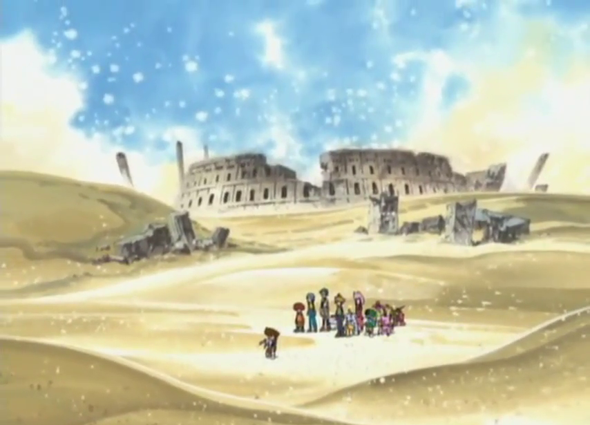 Screenshot of a frame showing the ruins of an amphitheatre-like structure along with other classical architectural elements in a sandy desert landscape -now even more ruined